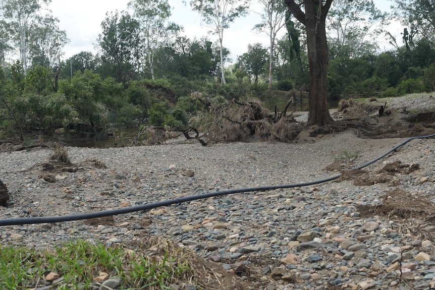 An expanse of river stones at the edge of an eroded creek. A length of irrigation piping sits exposed on the ground. 