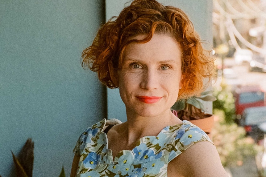 A woman with red hair leaning on one elbow on a balcony