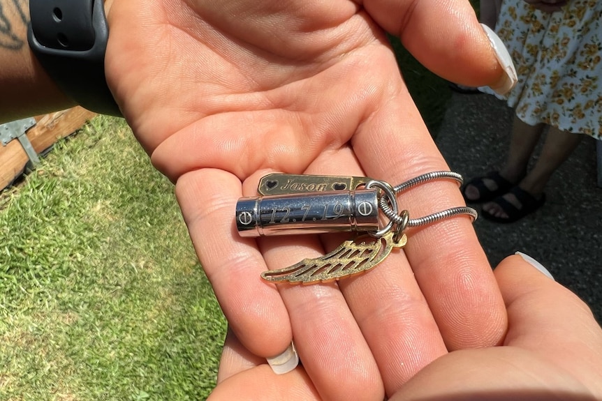 A woman's hand holding a silver and gold necklace with a locket engraved with 'Jason'