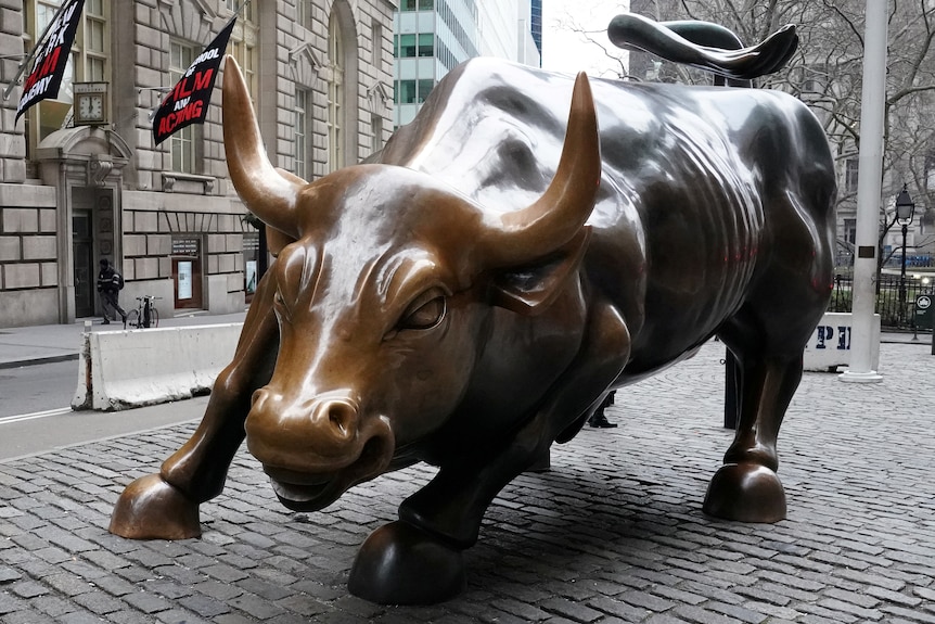 A statue of a bull charging sits on a paved city street