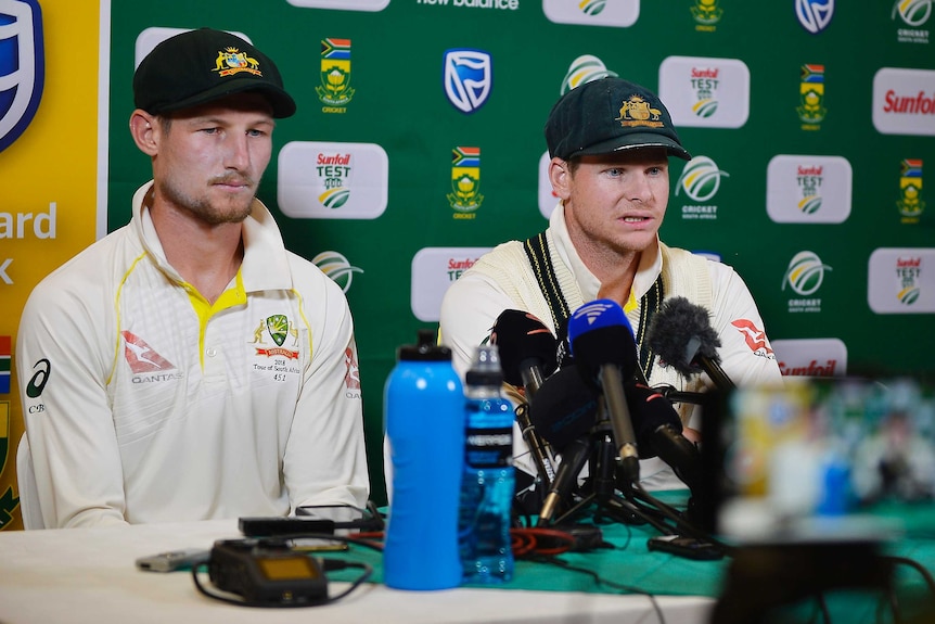 Tight shot of two male cricketers sitting and speaking at a press conference.
