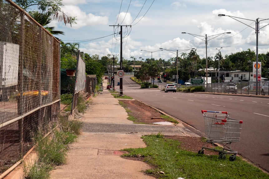 Static of a hot arterial road without trees. An abandoned shopping trolly in the foreground.