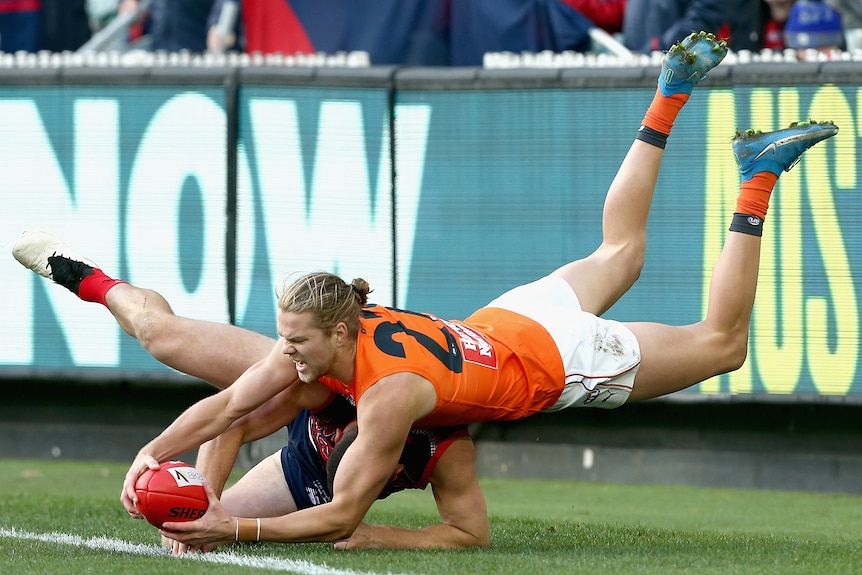 A GWS Giants AFL player dives to take possession of the ball against Melbourne.