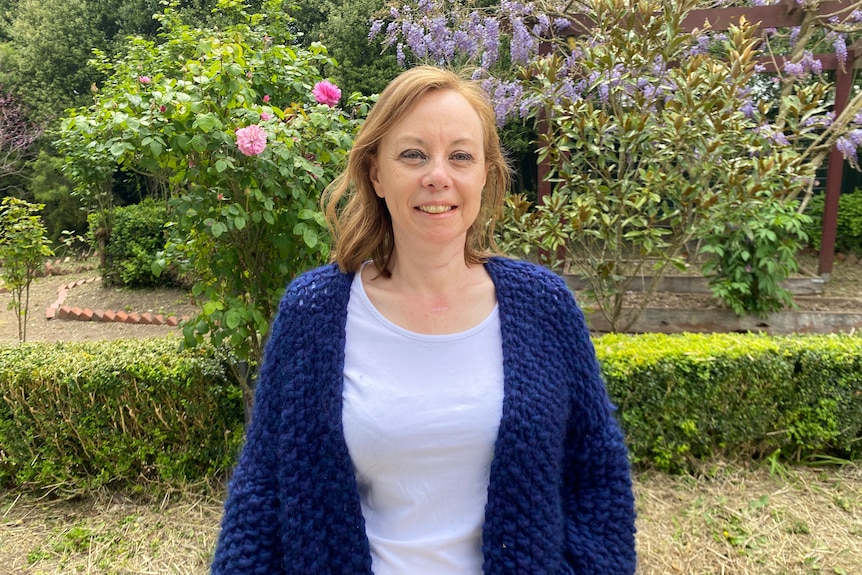 Woman wearing a blue shirt and cardigan, standing in a garden.
