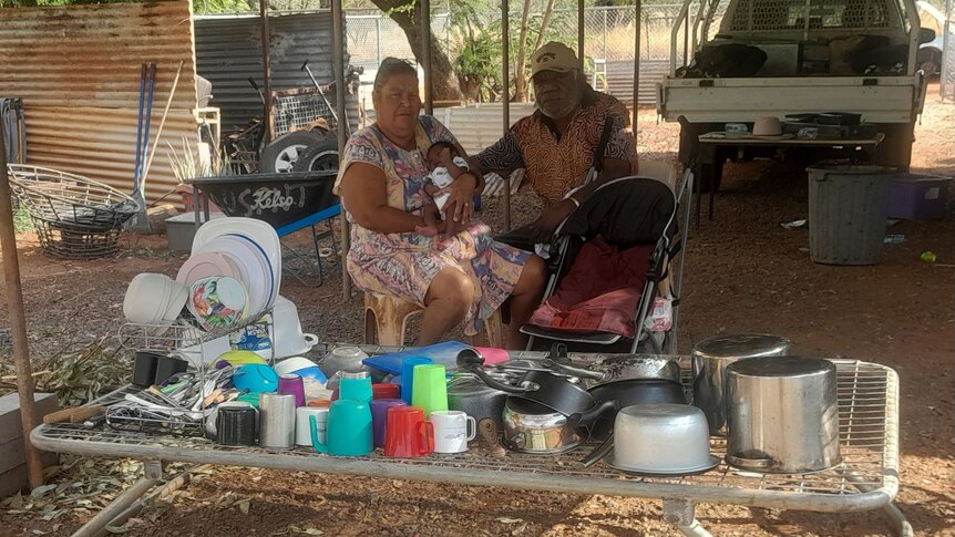 an aboriginal couple with a baby behind a table of cups and bowls