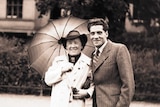 Black and white photo of a woman and man outside, woman holding umbrella.