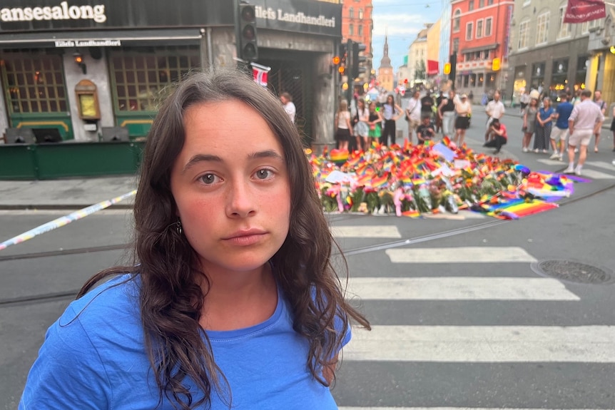 一位站在鲜花和彩虹旗前的妇女为受害者留下的纪念
