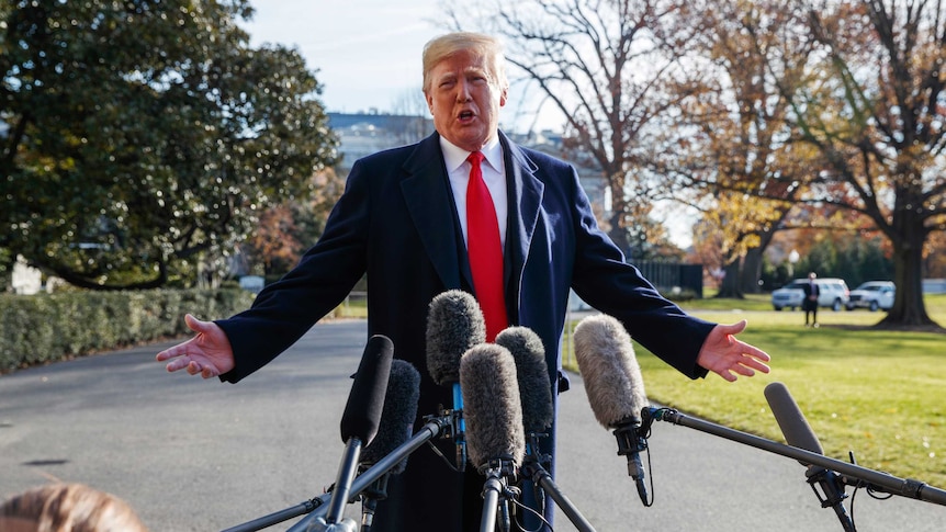 President Donald Trump speaks as reporters hold microphones