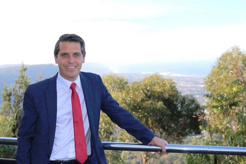 A man in a suit looks at the camera with his hand on a railing