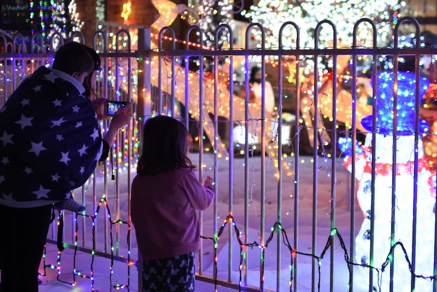A mother and children look at Christmas lights in a suburban front yard.