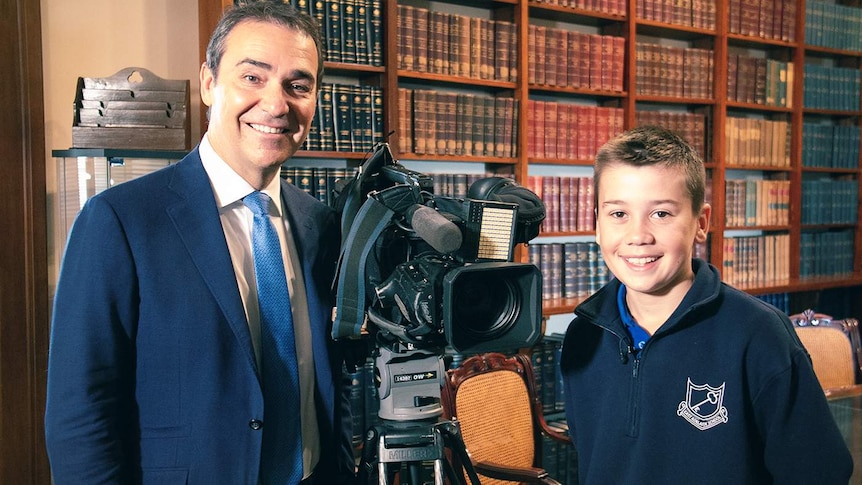 A boy stands with SA Premier Steven Marshall and camera on a tripod.