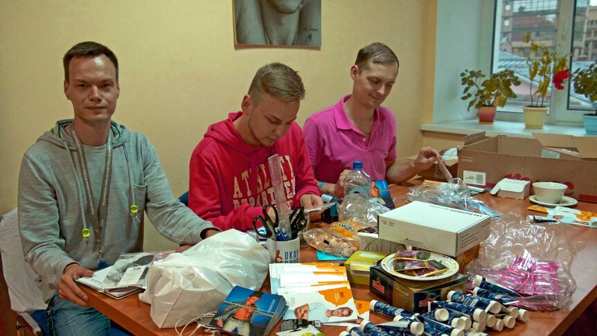 Three Russian men sit at a table preparing sexual health kits to deliver to gay clubs in Moscow.