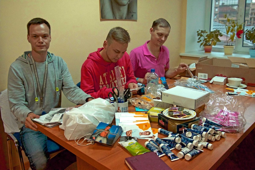 Three Russian men sit at a table preparing sexual health kits to deliver to gay clubs in Moscow.