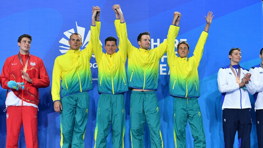 Gold medallists Kyle Chalmers, Jack Cartwright, James Magnussen and Cameron McEvoy raise their arms on the podium.