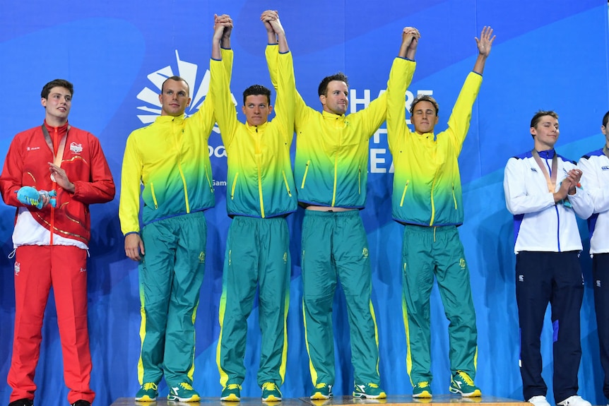 Gold medallists Kyle Chalmers, Jack Cartwright, James Magnussen and Cameron McEvoy raise their arms on the podium.