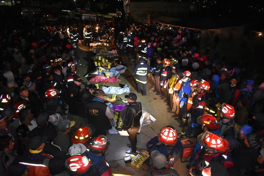 A large crowd watches as emergency services personnel  work at the scene of a fatal truck crash