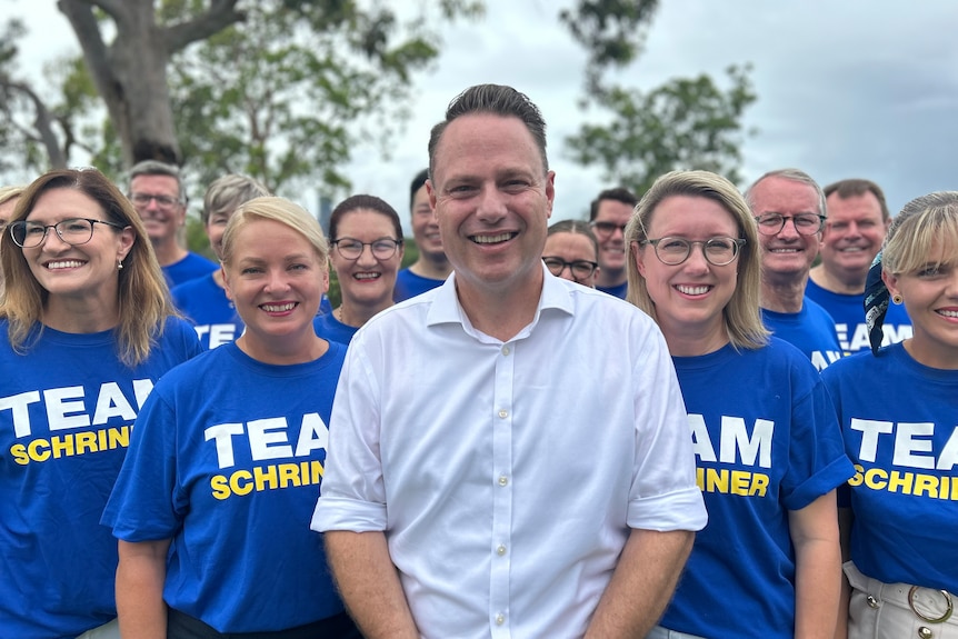 A man wearing a white shirt surrounded by people wearing blue shirts branded with 'Team Schrinner'
