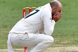 Nathan Lyon holds his head in his hands while squatting down next to the wickets