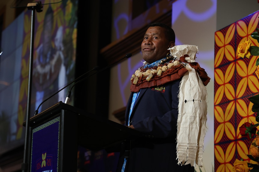 Fijian man stands on stage speaking into microphone at an awards night. 