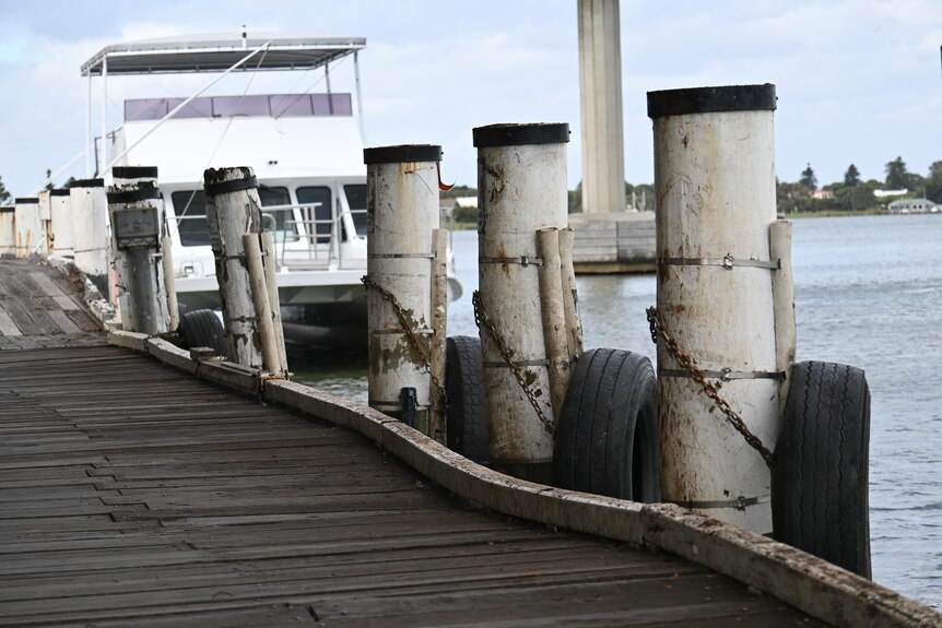 A uneven old wharf on the Murray River with a tourist boat moored in the distance
