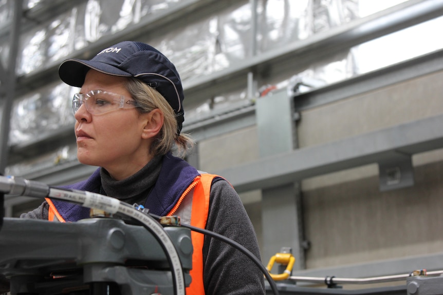 A woman looks serious as she inspects some parts of the train she is helping to build. 