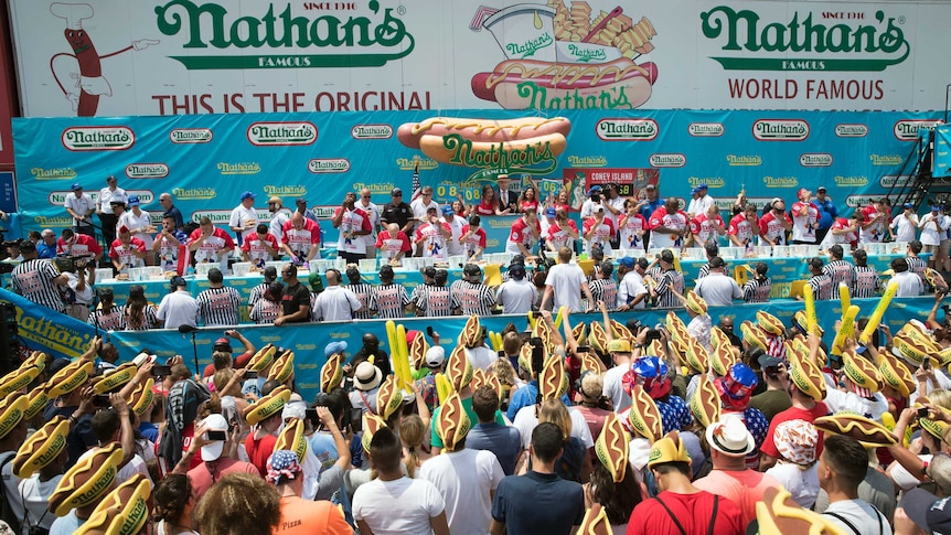 Fans wearing hot dog hats watch the male contestants