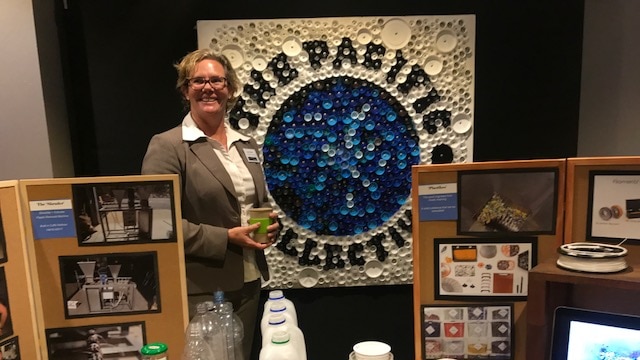 Louise Hardman standing before an artwork made from plastic coffee cup and water bottle caps. Coffs Harbour, June 18, 2017.