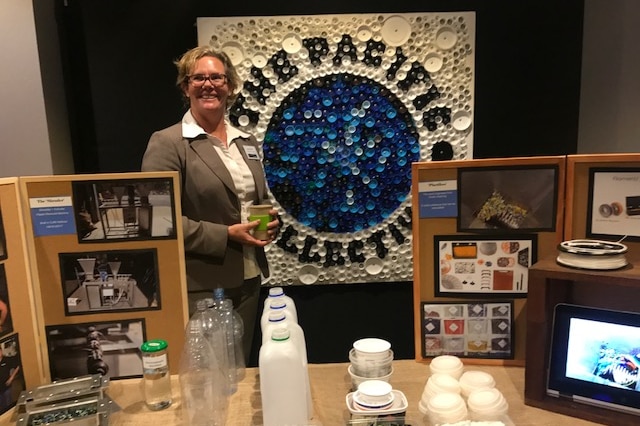 Louise Hardman standing before an artwork made from plastic coffee cup and water bottle caps. Coffs Harbour, June 18, 2017.