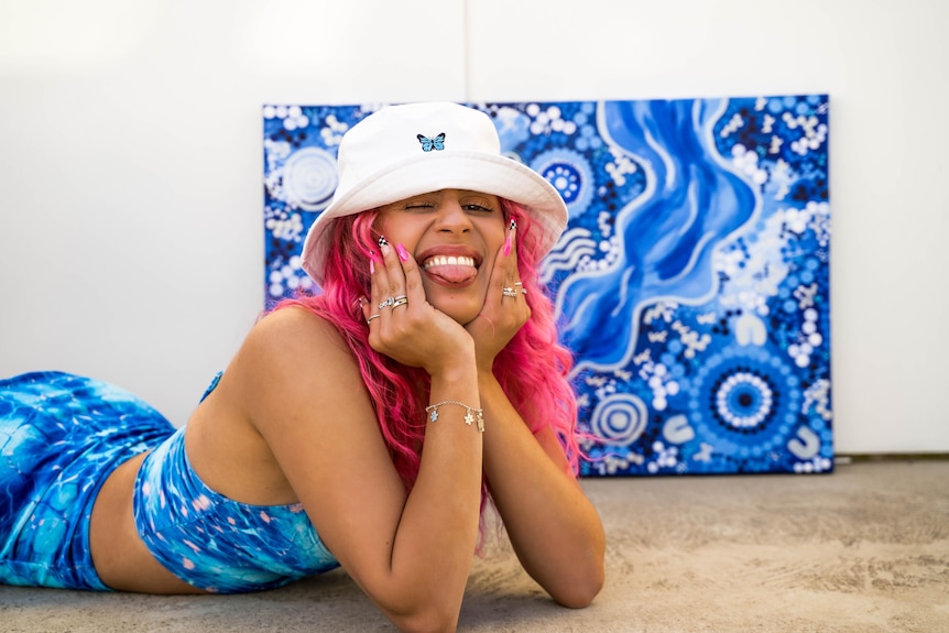 a smiling girl in a bucket hat in front of a blue artwork