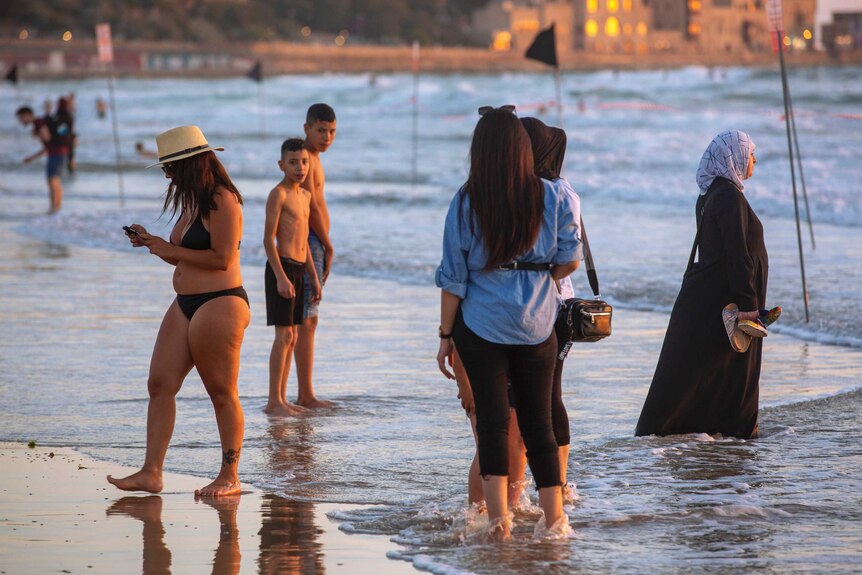 People in swimwear stand in the shallows at a beach