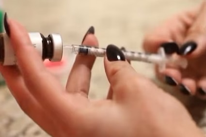 Hands with dark nail polish drawing up an injection.