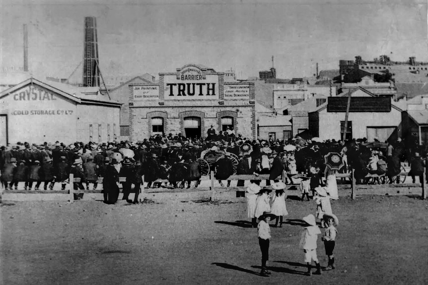 A black and white archive image of people gathering around a building that has a sign reading Barrier Truth