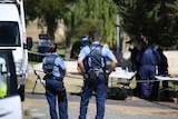 Police stand in front of a cordon, with forensic officers in the background.