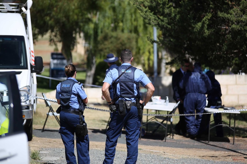 Police stand in front of a cordon, with forensic officers in the background.