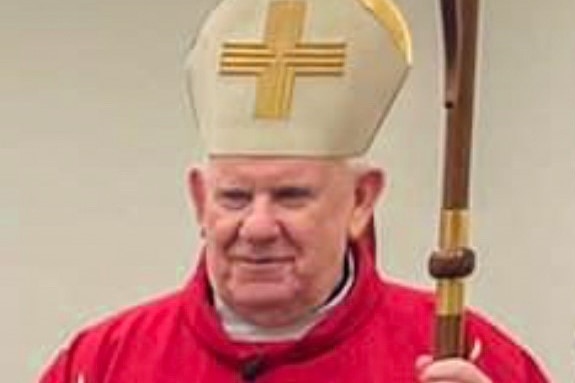 a man in a red cloak where's a hat with a crucifix on it and holds a staff
