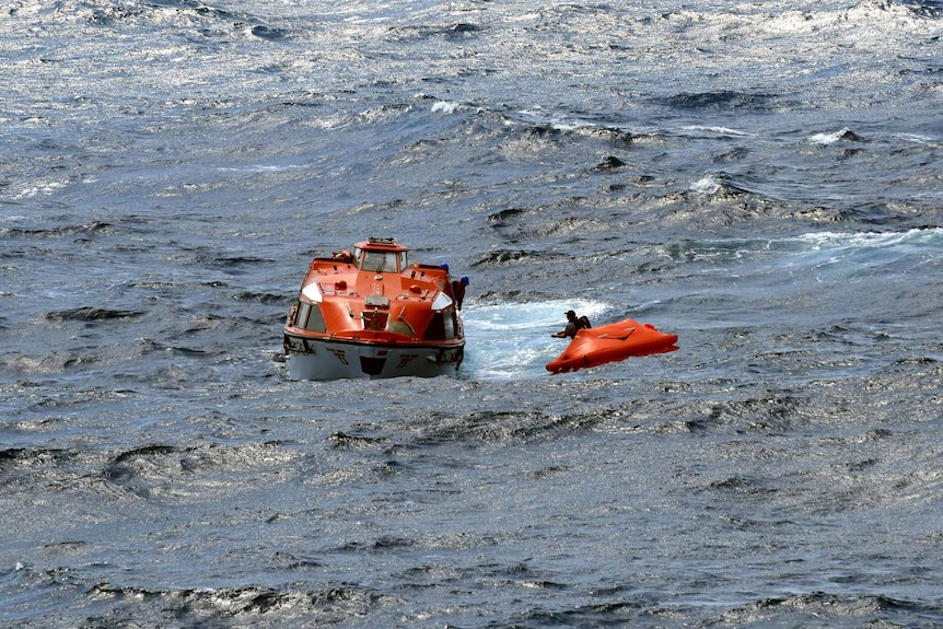 A rescue boat is beside a small life raft at sea