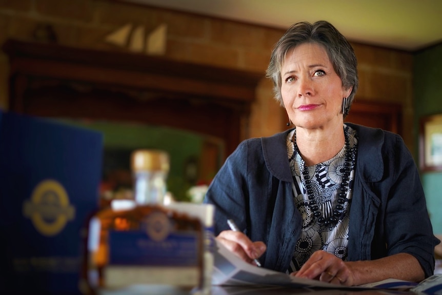 A woman sits at a table holding a pen