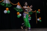 Indian man in vibrant green, gold and blue costume performing a dance on stage