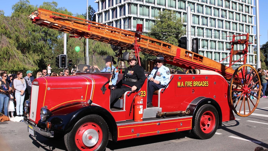 A bright red historic fire truck carrying three veterans in the Anzac Day parade.