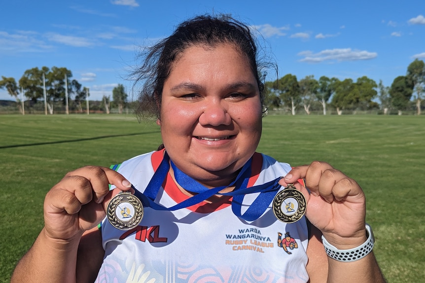 A young woman stands delighted with two medals on Purkiss Reserve