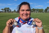 A young woman stands delighted with two medals on Purkiss Reserve