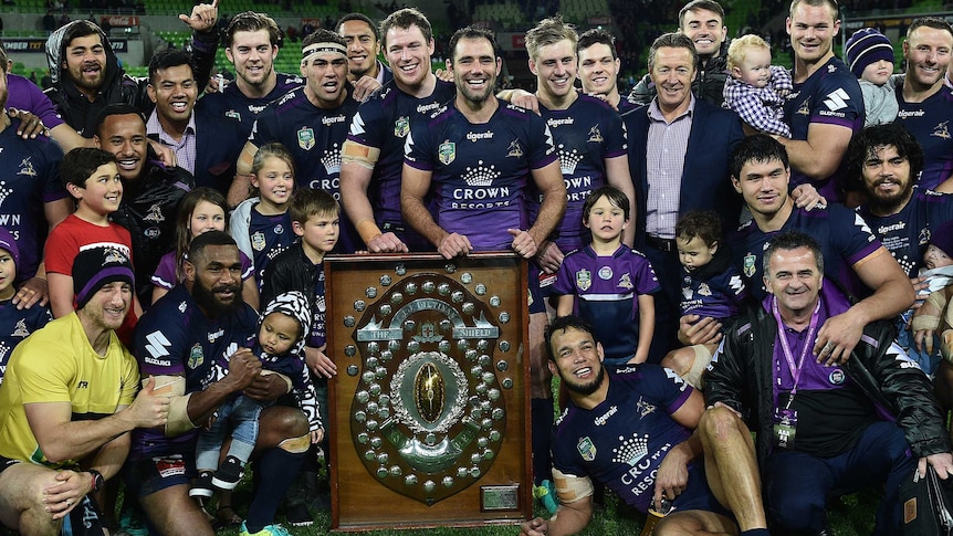 Players, family and officials of the Storm celebrate around the minor premiership shield in September, 2016.