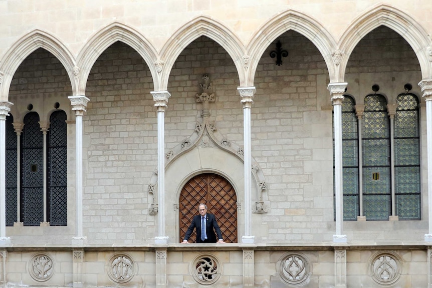 A man clad in a suit and tie stands in the verandah of a historic building.