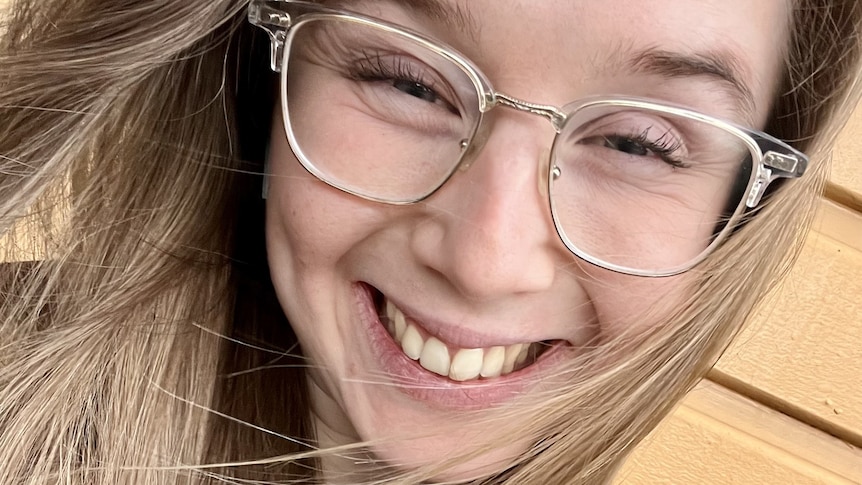 A close up of a young woman smiling, wearing glasses. 