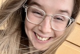 A close up of a young woman smiling, wearing glasses. 
