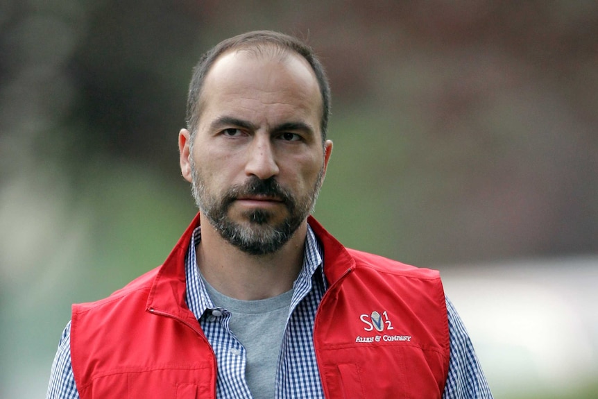 Head and shoulders shot of bearded, balding man wearing check shirt and orange vest.