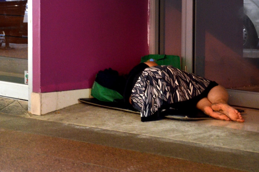 A homeless woman lies in the doorway of a business.