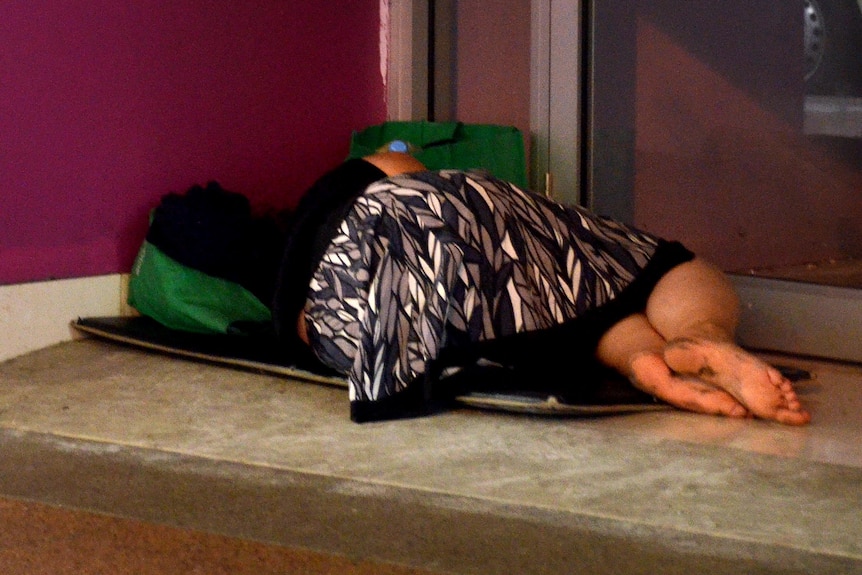 A homeless woman lies near a storefront.