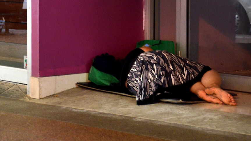 A homeless woman lies in the doorway of a business.