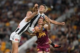 A Collingwood player leaps high and punches the ball clear as he is one of three players grimacing in a contest.